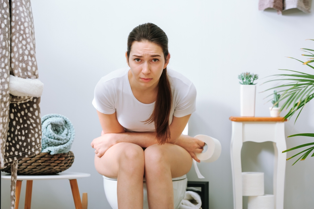 Young,Woman,Suffering,From,Constipation,On,Toilet,Bowl,At,Hom